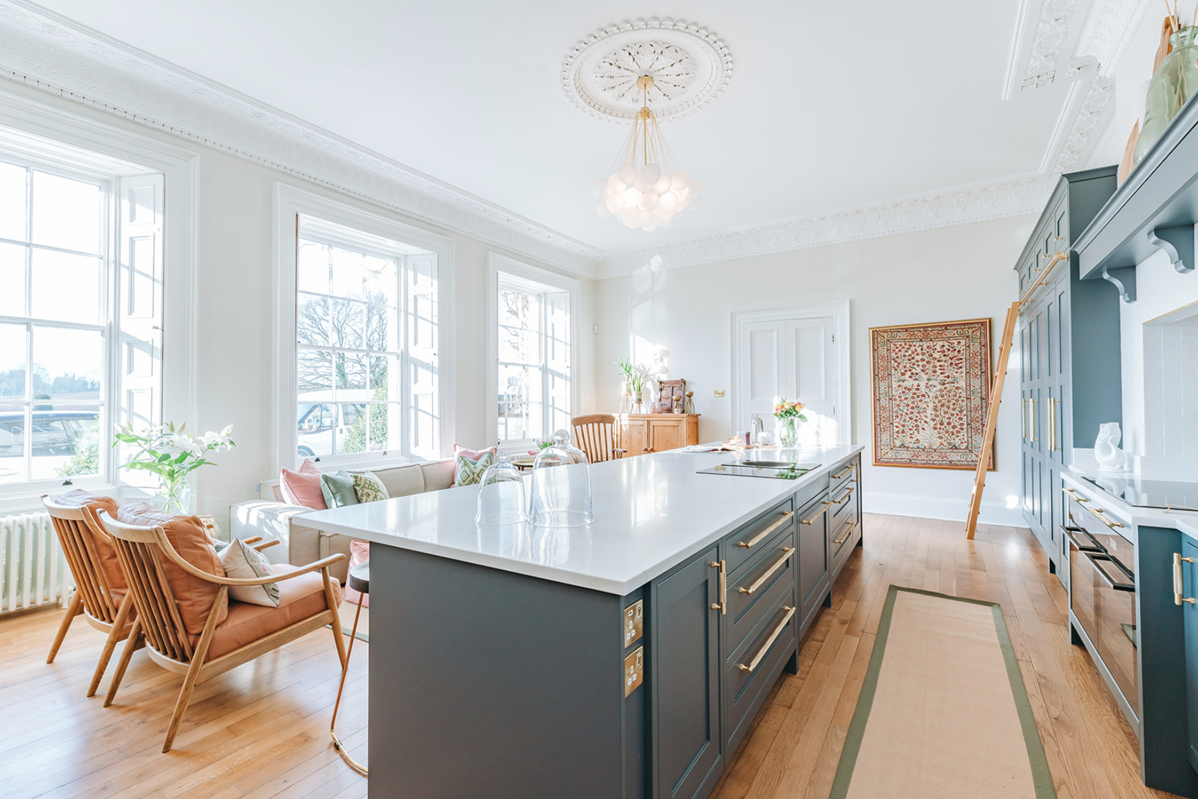 Grand period kitchen with a dark blue island, original cornice and ceiling rose, tall sash windows and a brass library ladder