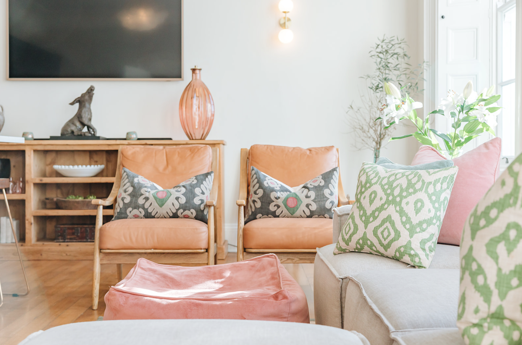 Sitting room with tan leather armchairs, patterned cushions and a brass wall light beside panelled shutters