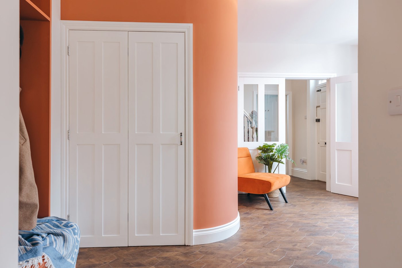Curved terracotta hallway with built-in coat storage, a glazed screen to the staircase and a herringbone tiled floor