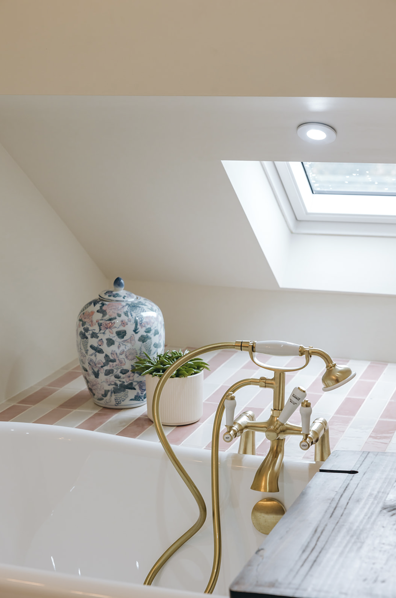 Attic bathroom with a freestanding bath beneath a skylight, brass telephone mixer and pink and cream striped tiling