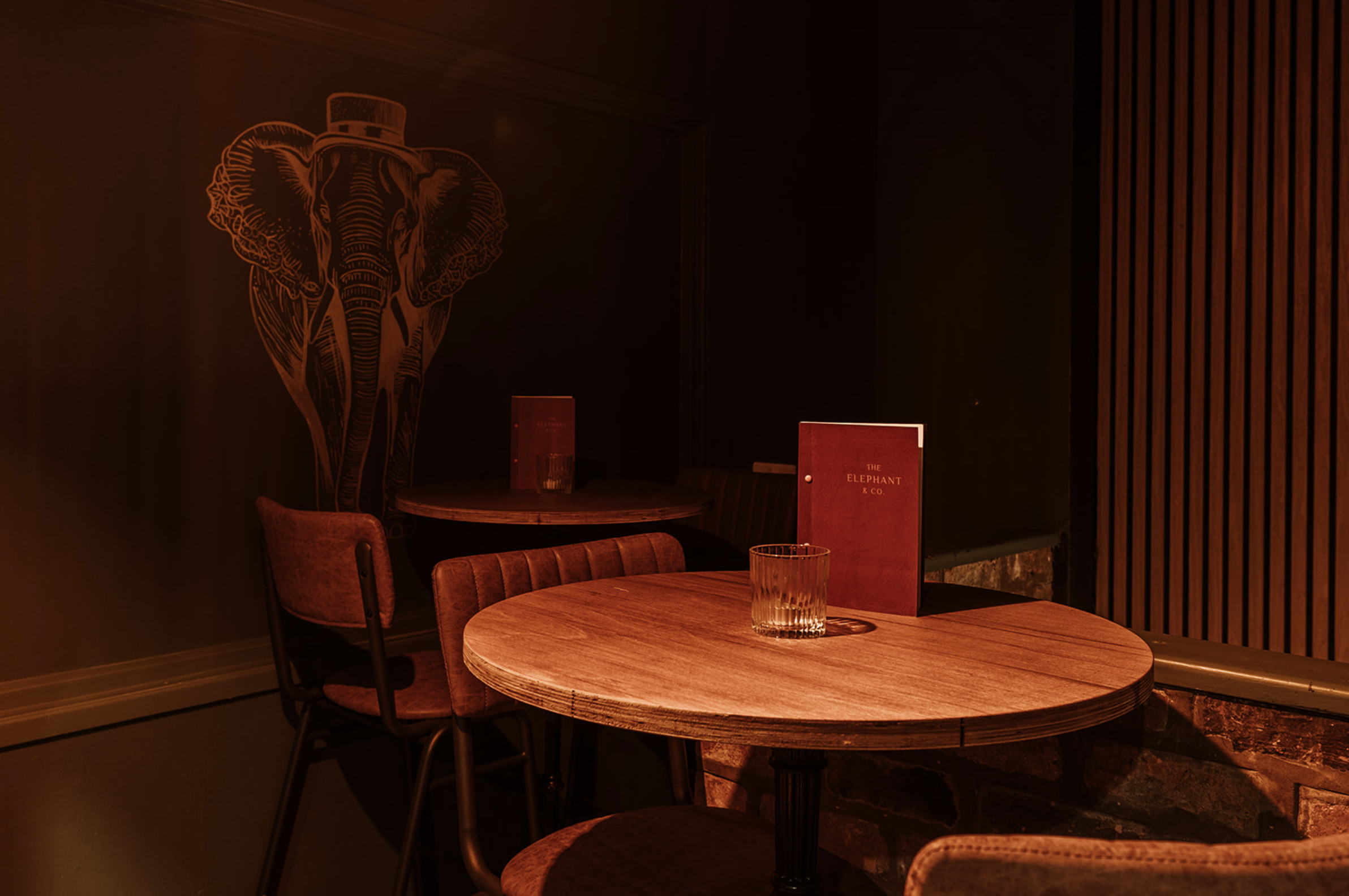 Low-lit corner table beneath the gold elephant mural with the Elephant & Co menu