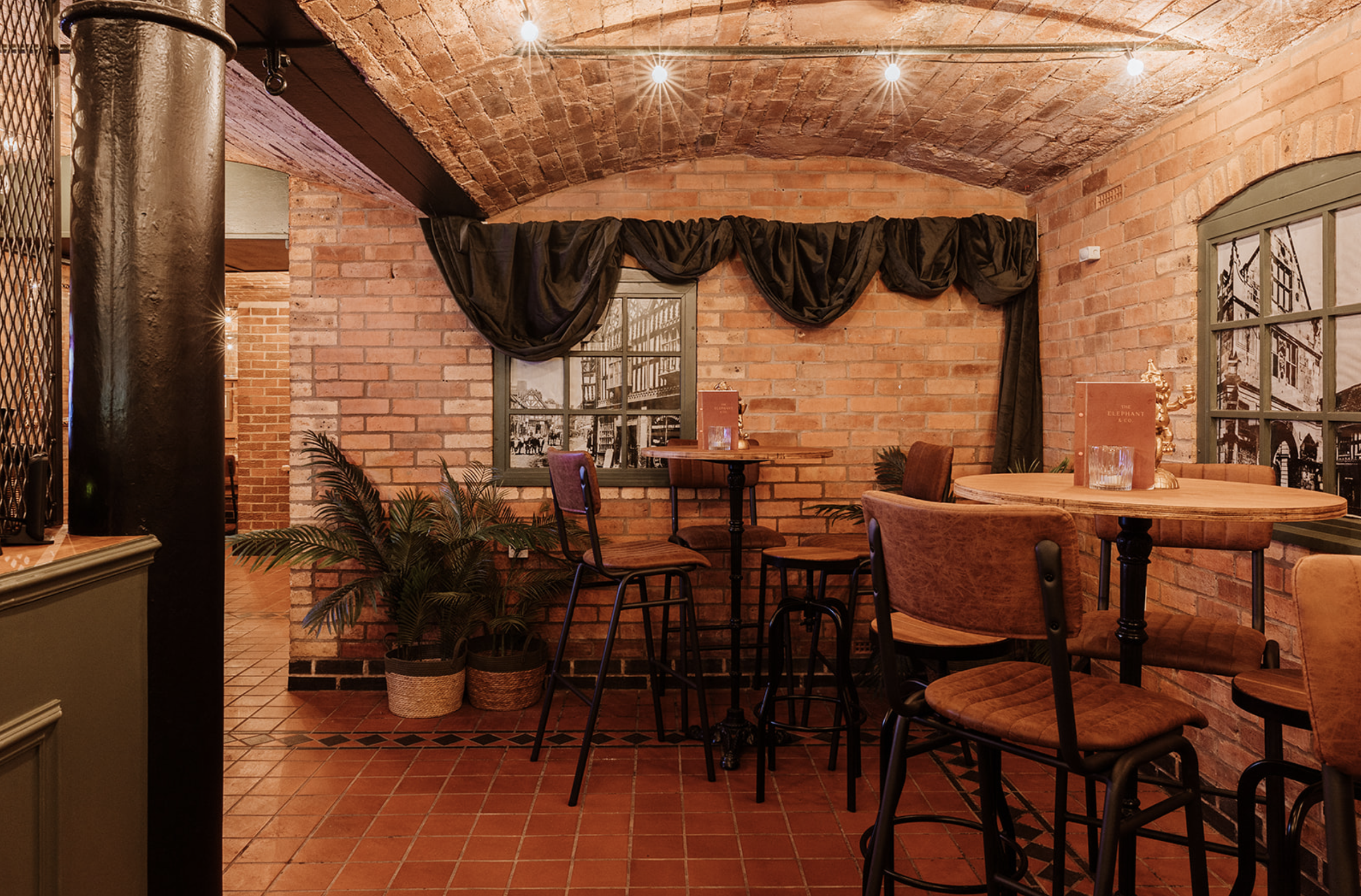 High tables and stools in a brick alcove at The Underground beneath festoon lighting