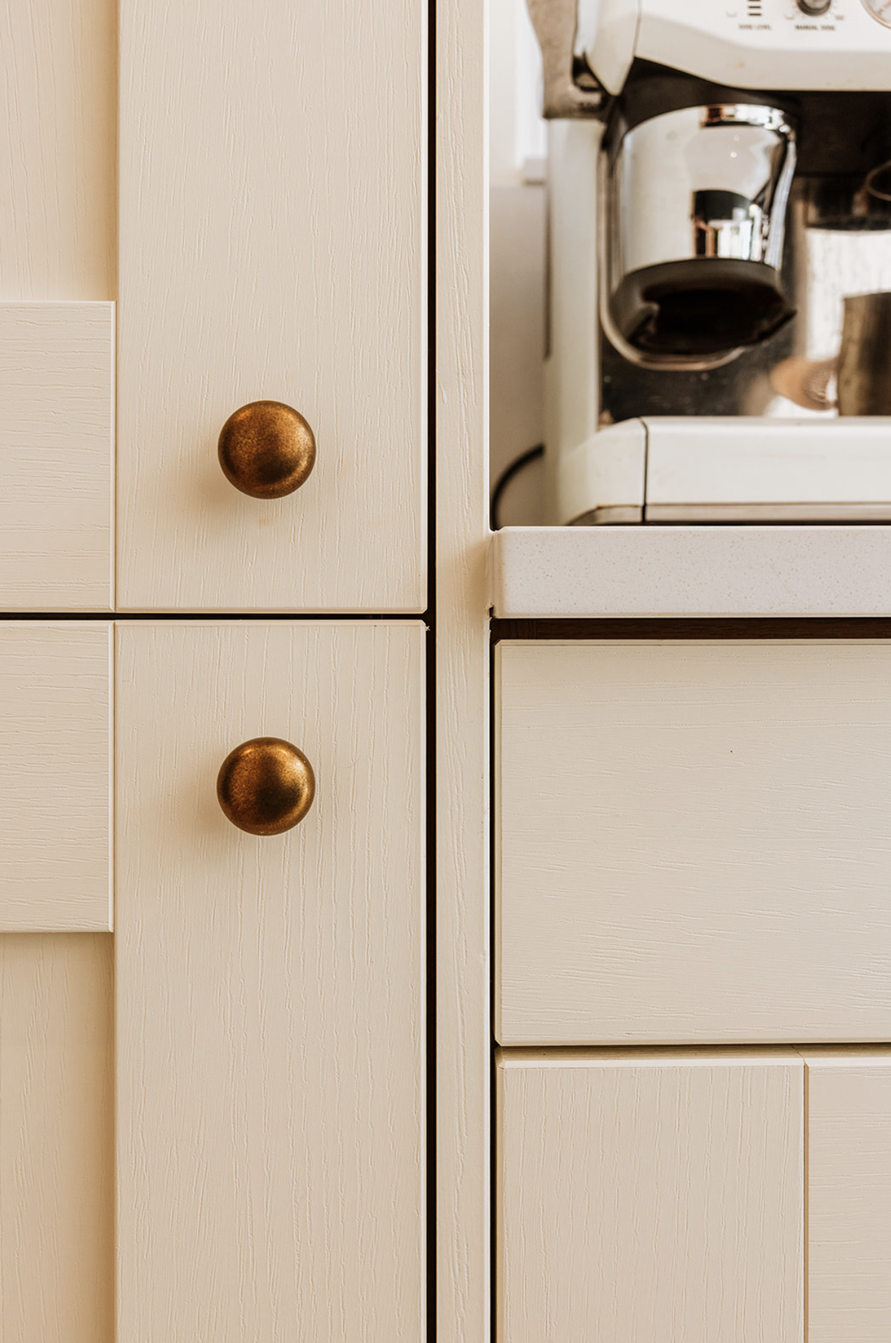 Cream cabinetry with aged brass knobs beside a coffee station
