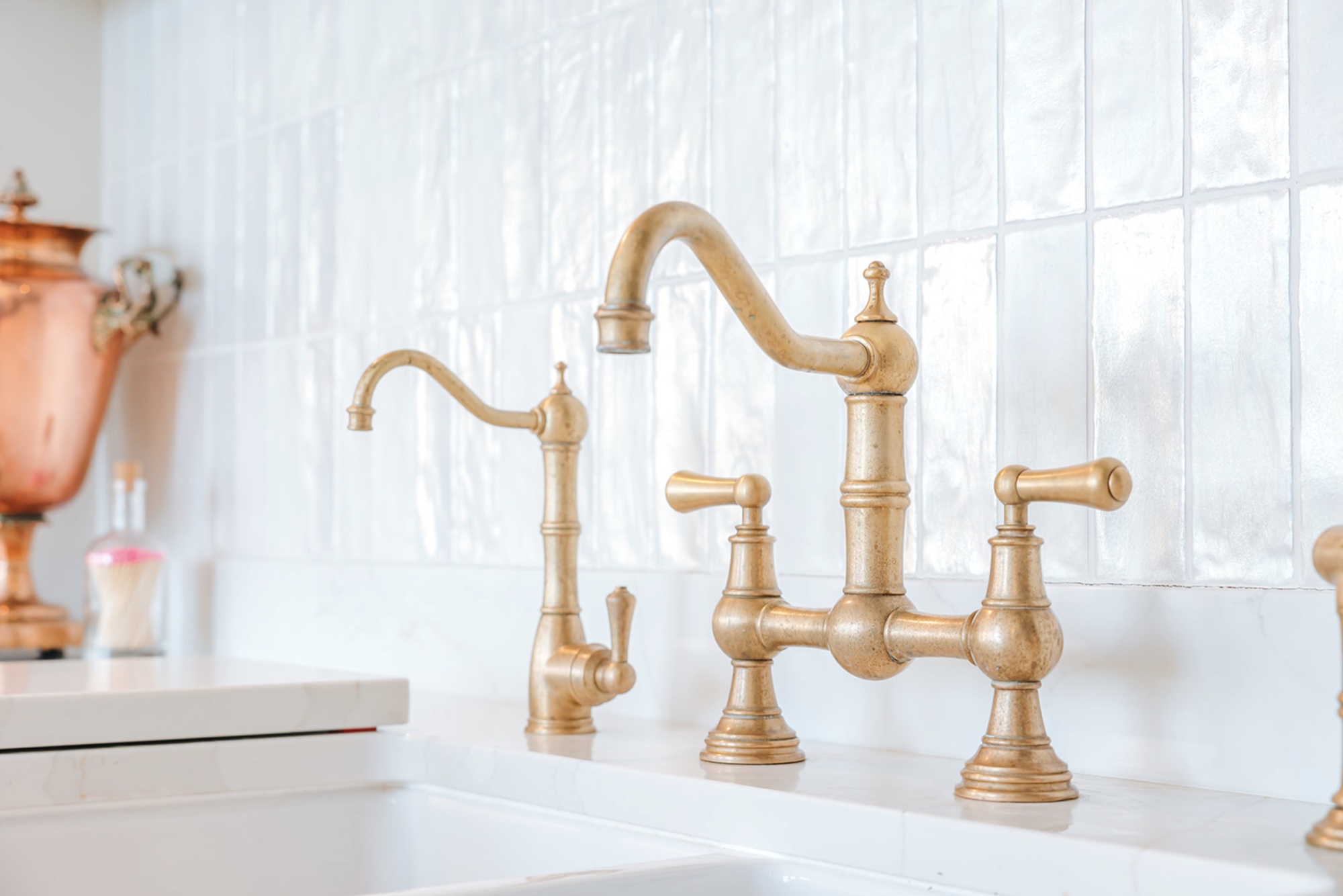 Aged brass bridge tap and separate rinse tap against softly rippled white tiles