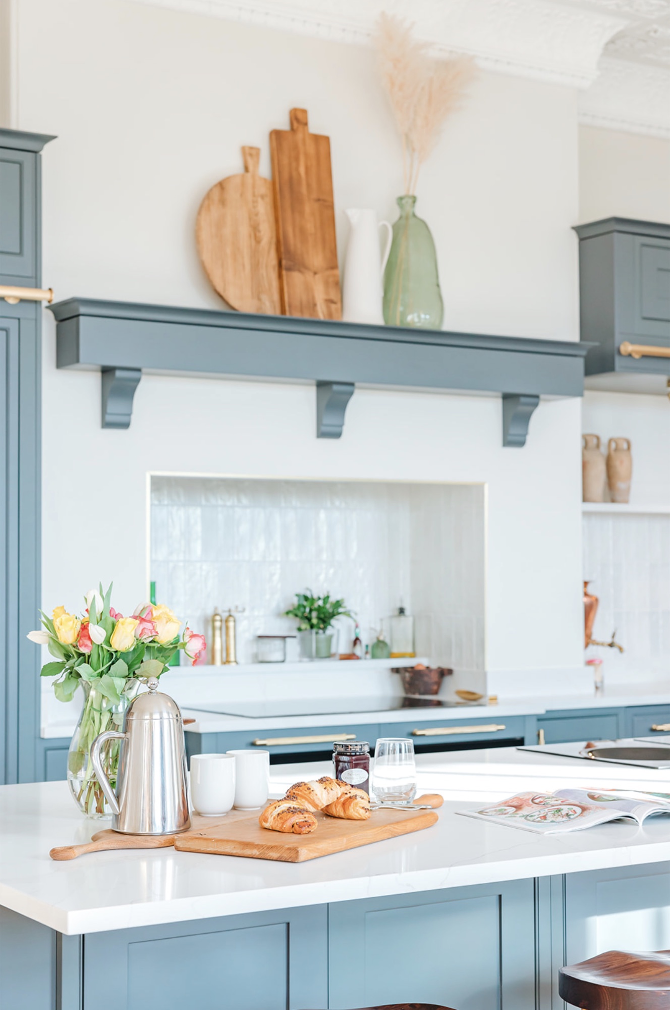 Breakfast with pastries and flowers on the white kitchen island, teal cabinetry beyond