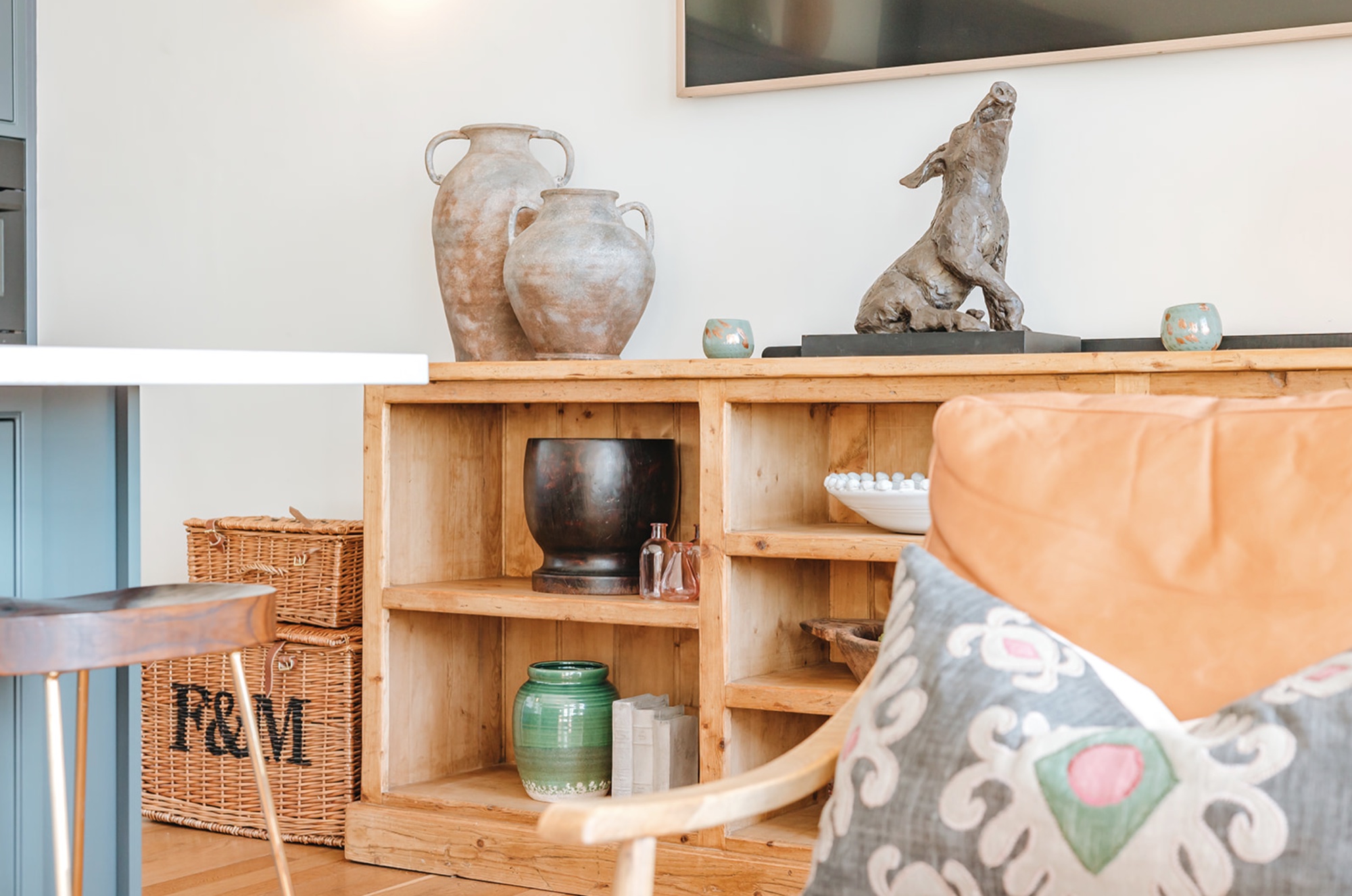 Low reclaimed timber cabinet with ceramics and sculpture beside a tan leather chair