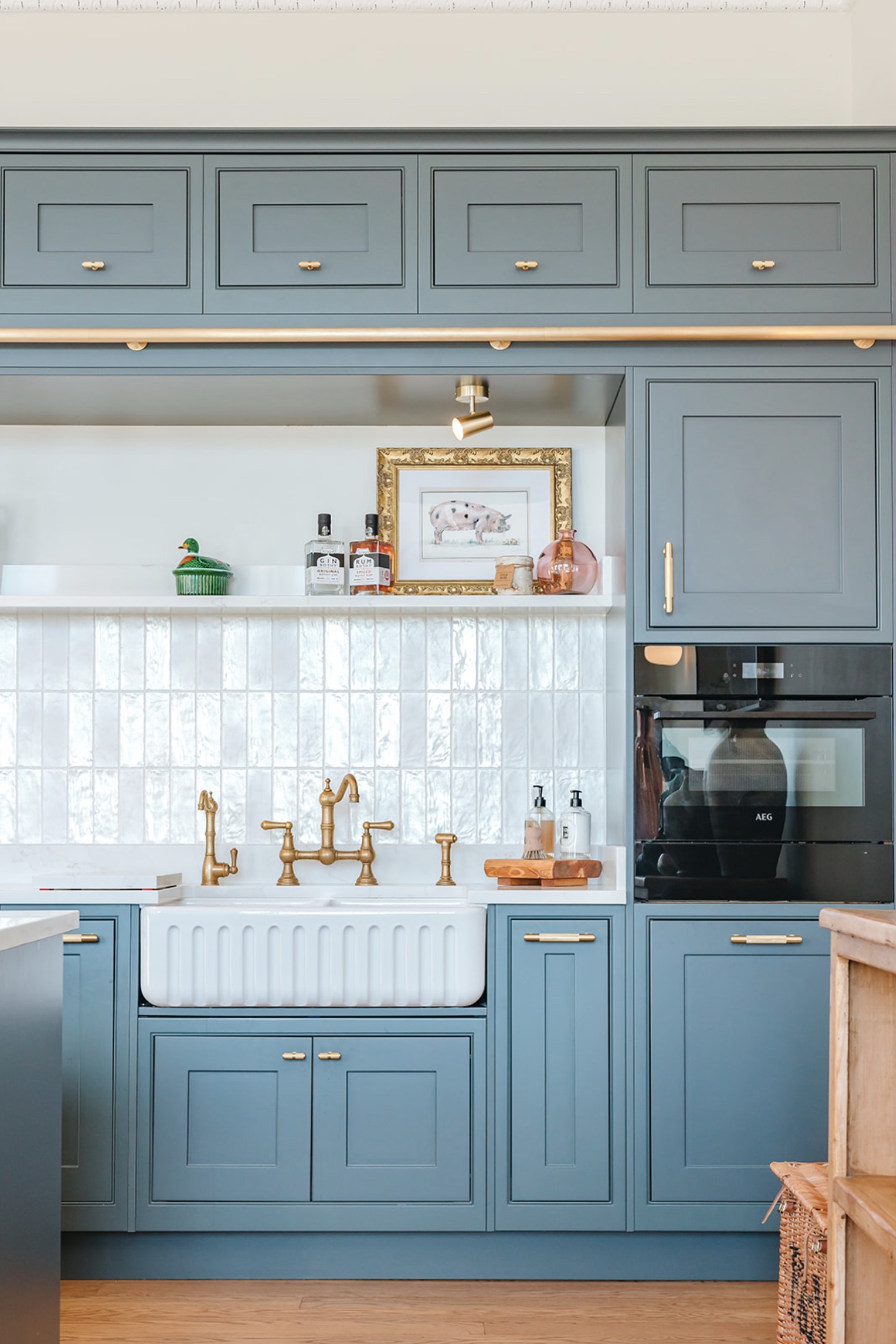 Teal kitchen cabinetry framing a white fluted butler sink, brass bridge tap and tiled splashback