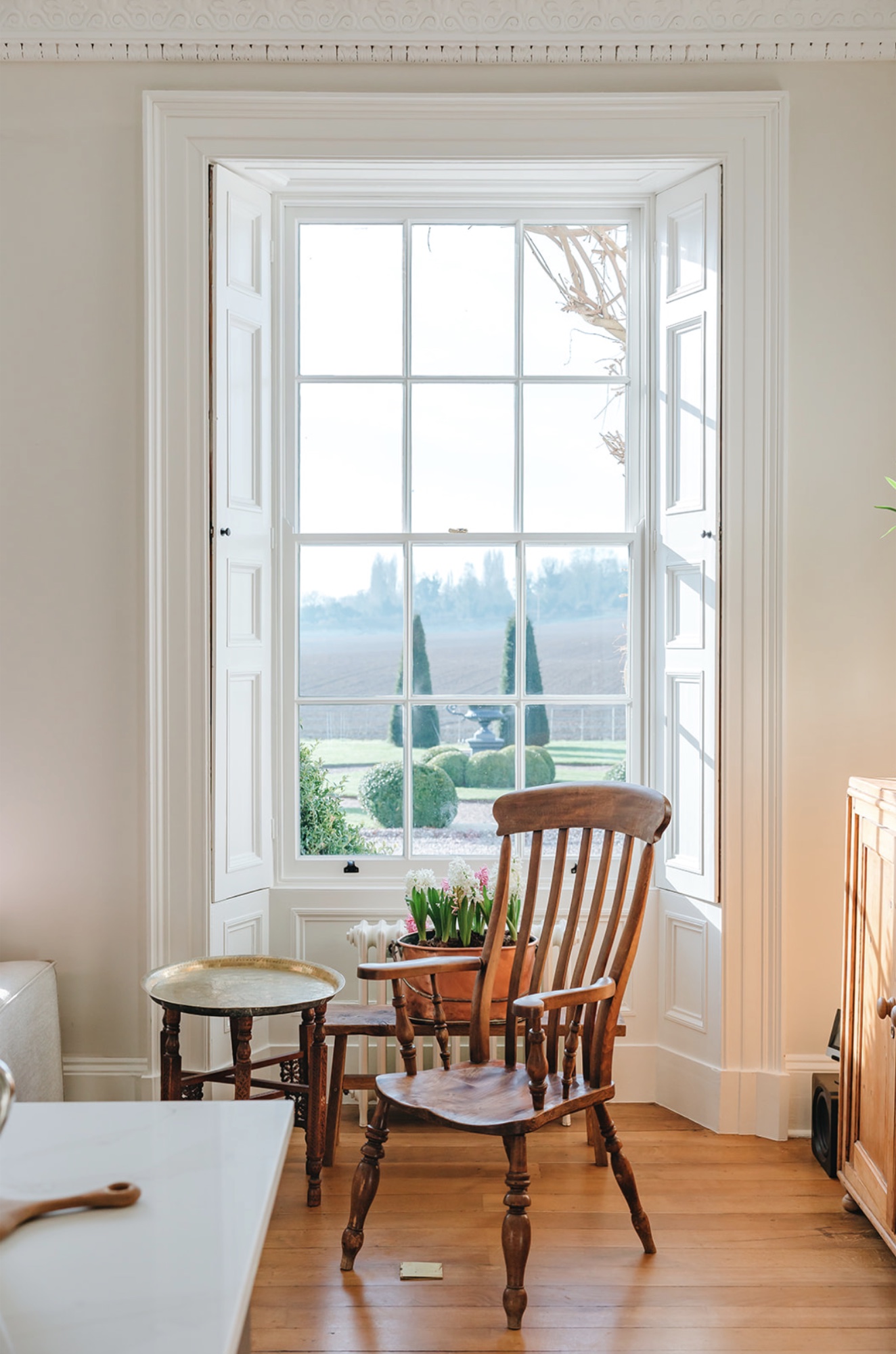 Antique wooden chair beside a tall shuttered sash window overlooking the formal gardens at Bicton Hall