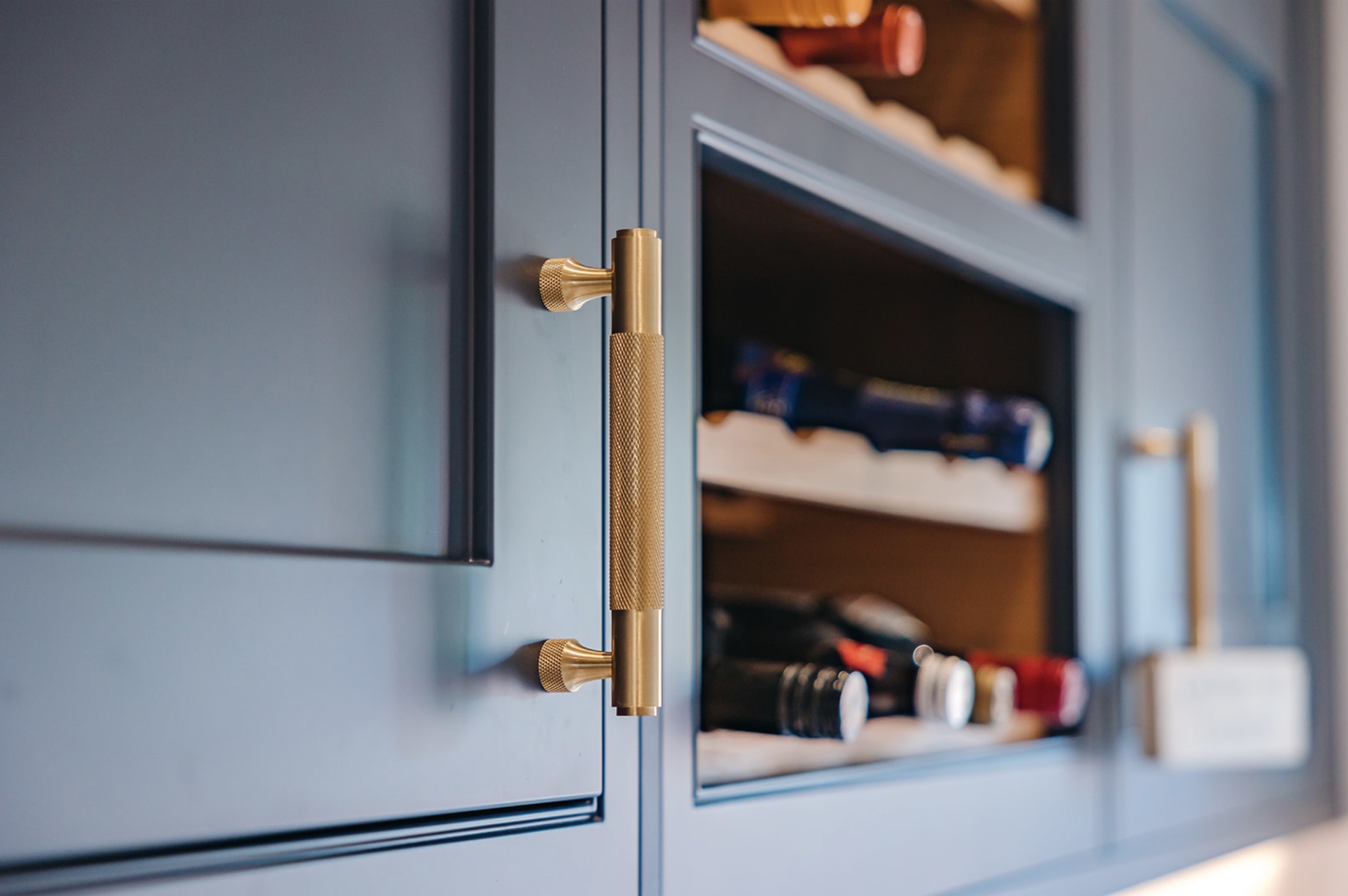 Knurled brass cabinet handle beside an integrated wine rack in teal joinery