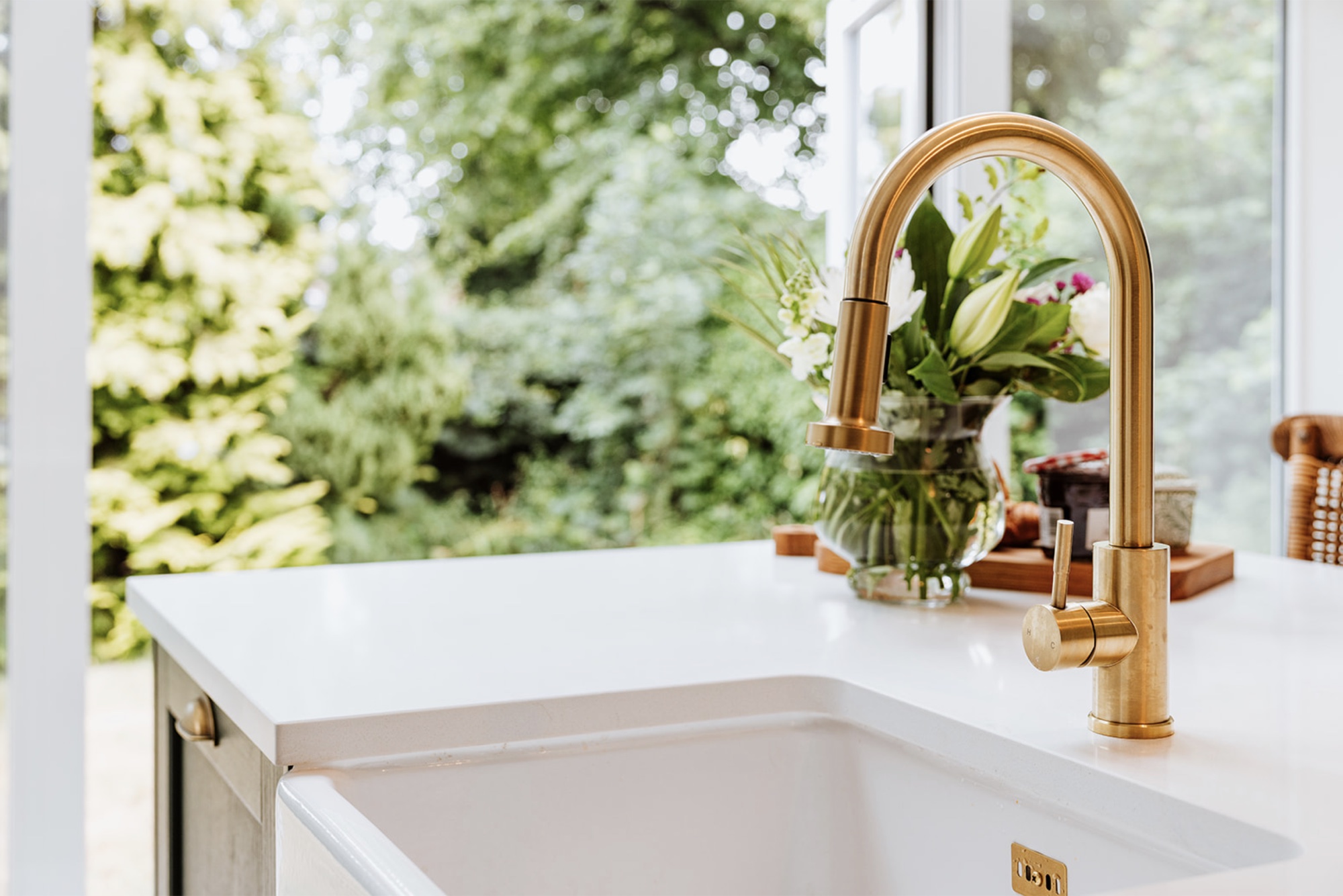 White kitchen sink and brushed brass tap facing the garden