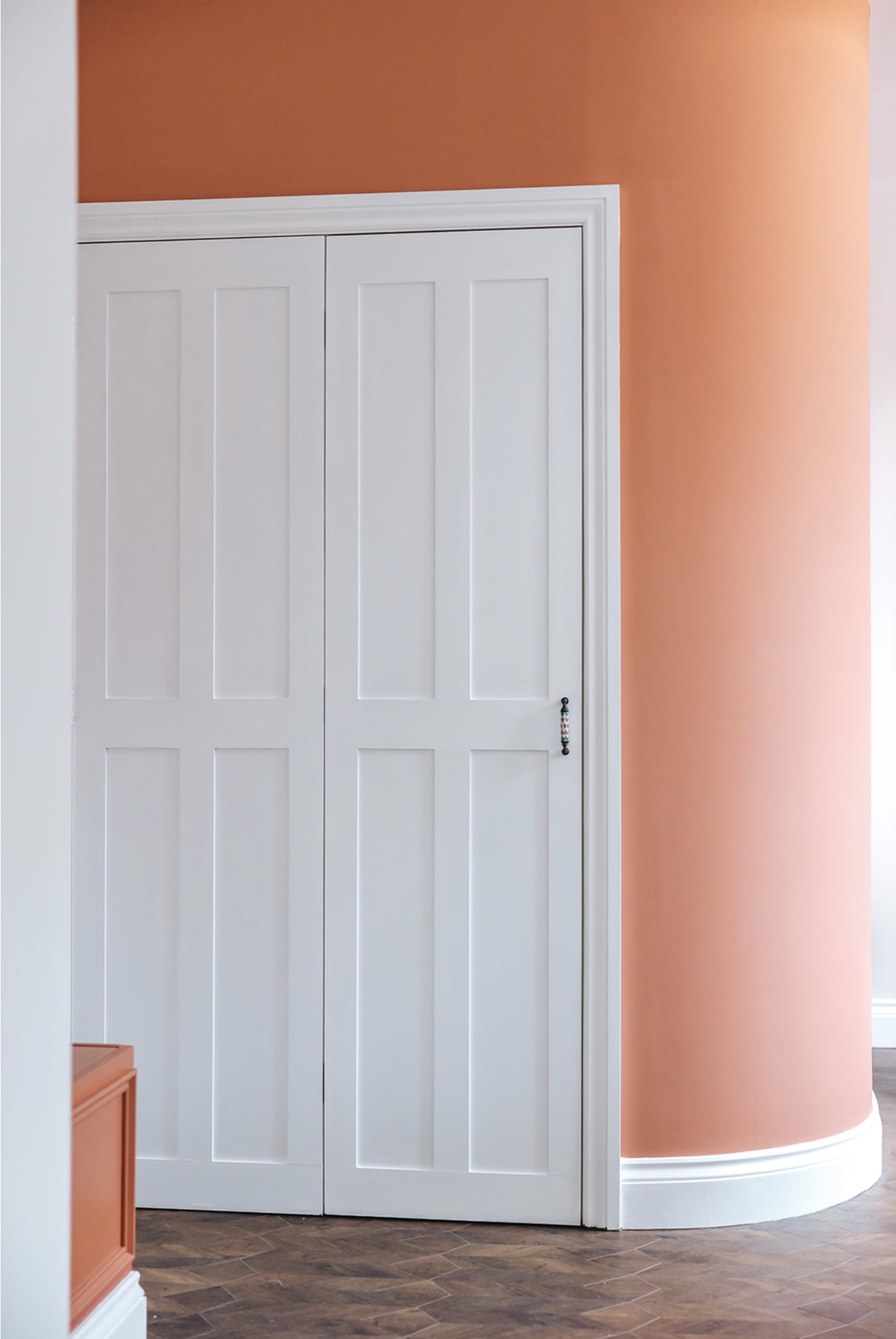 White panelled cupboard doors set into a curved terracotta wall above herringbone flooring