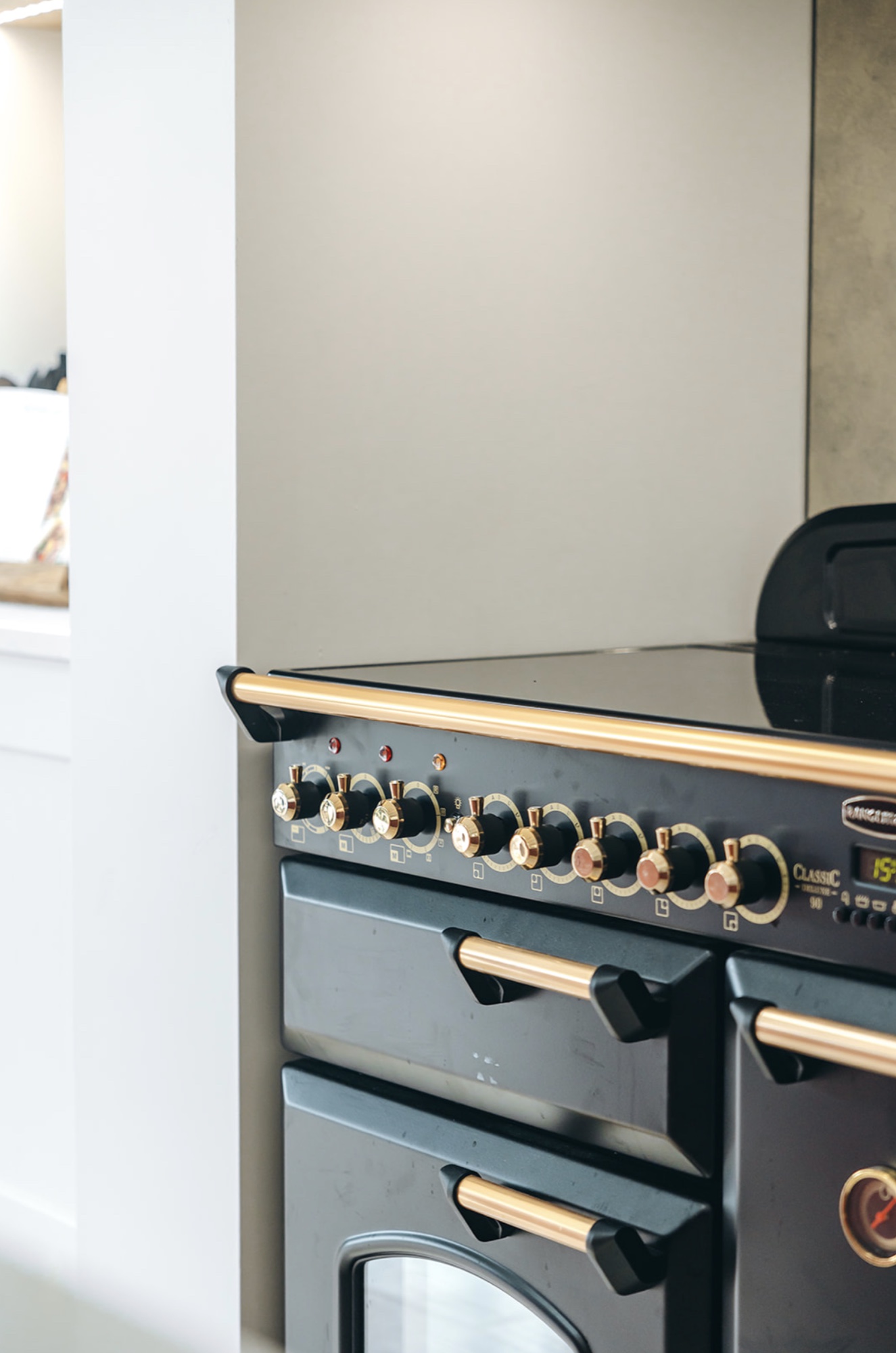 Black range cooker with brass controls and handles set into the pale kitchen