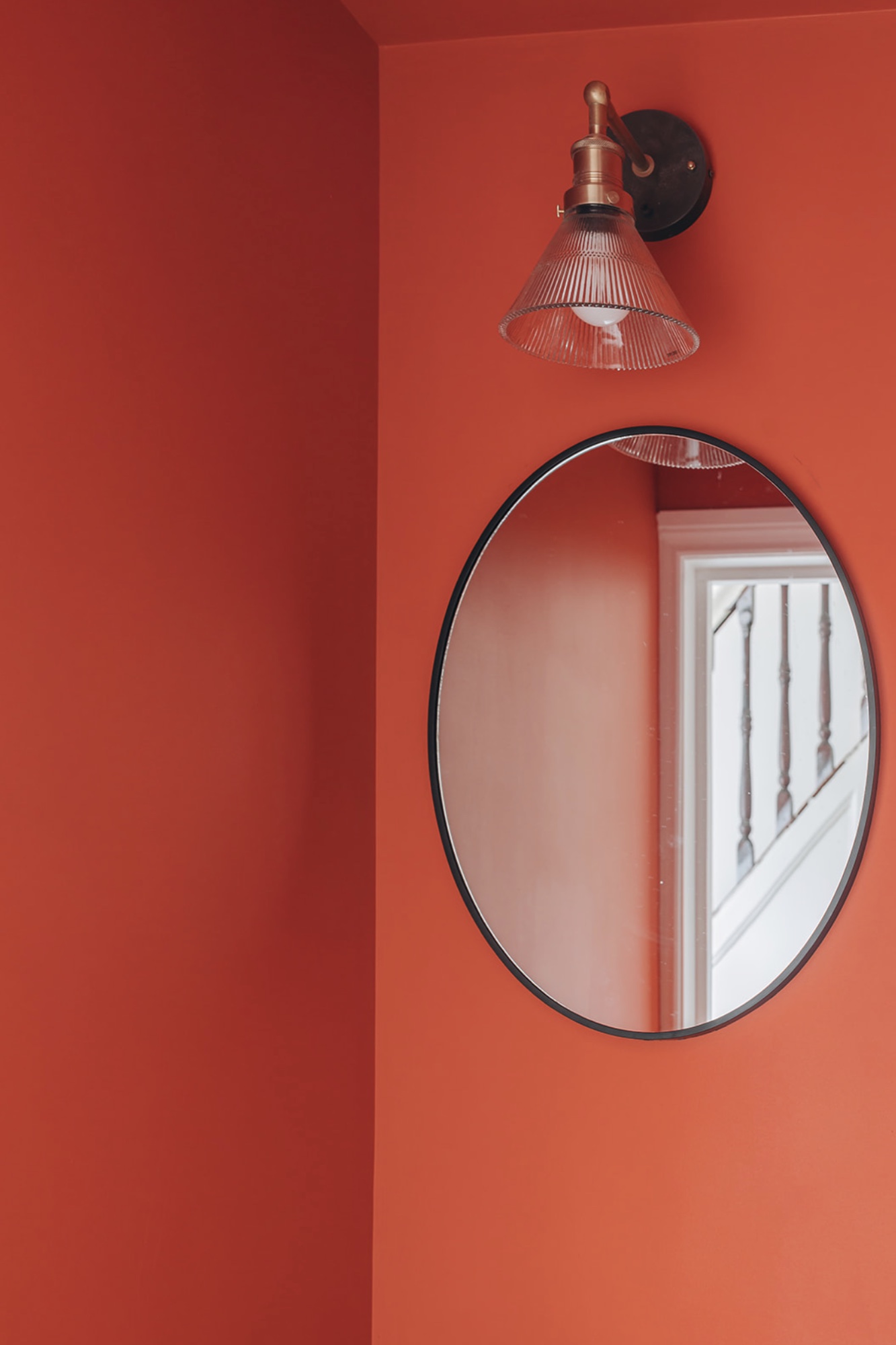 Oval black-framed mirror and ribbed glass wall light against a vivid red wall