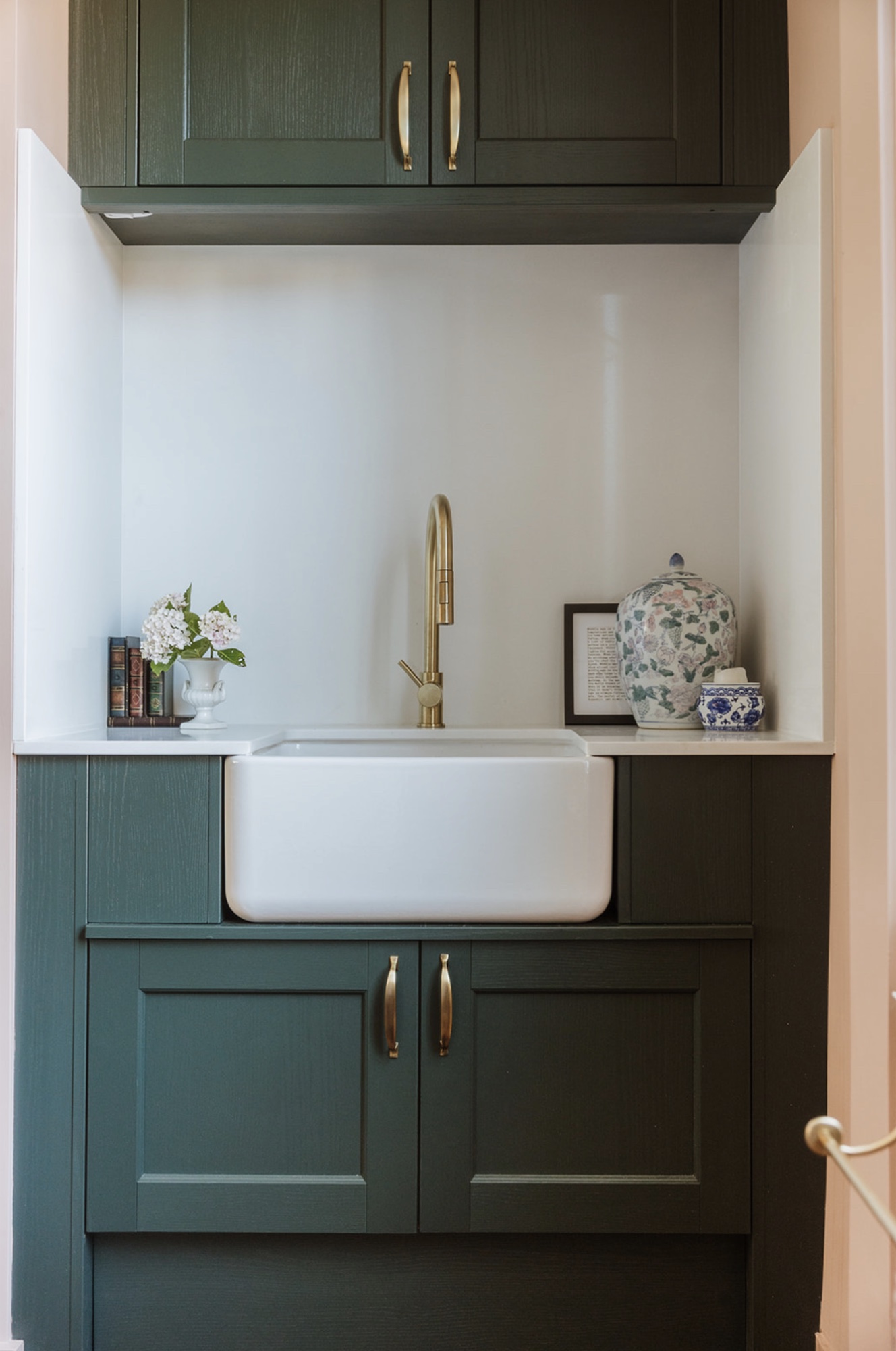 Bespoke deep green utility cabinetry with a white ceramic sink and brass tap