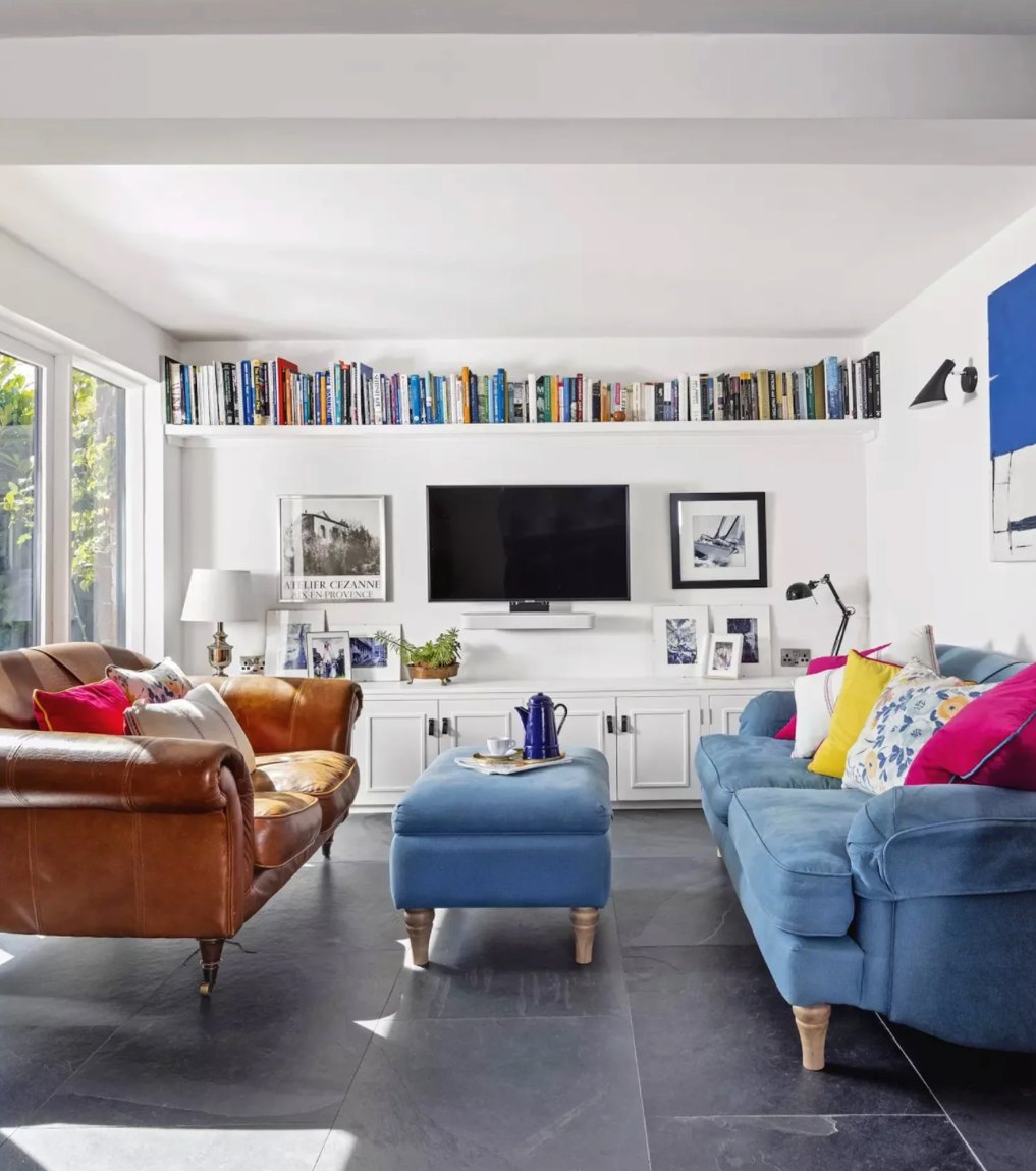 Family room at Oakleigh House with blue and leather sofas, a high book ledge, built-in cabinetry and slate floor