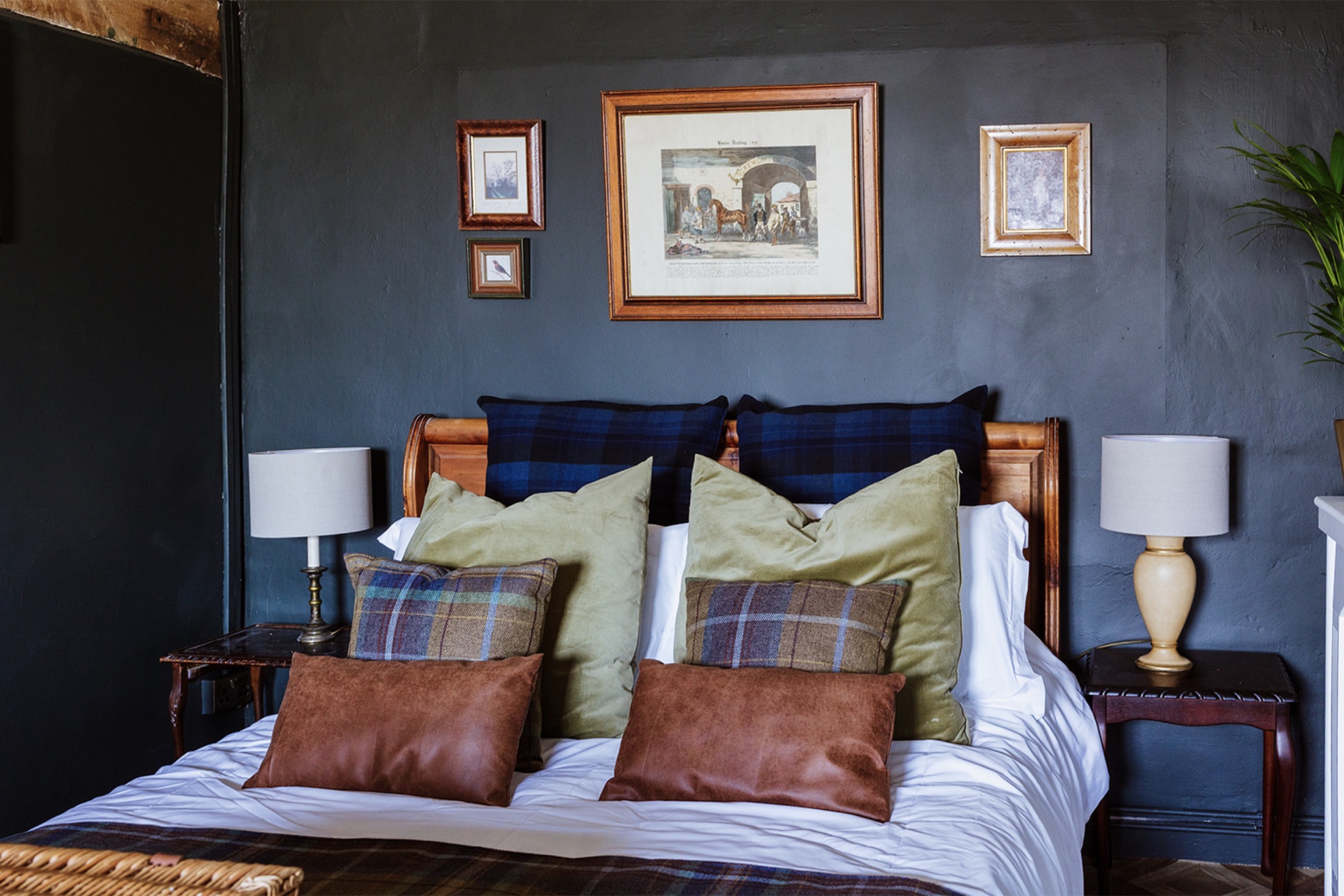 Detail of the Pool House bed with green, tartan and rust cushions against a dark wall