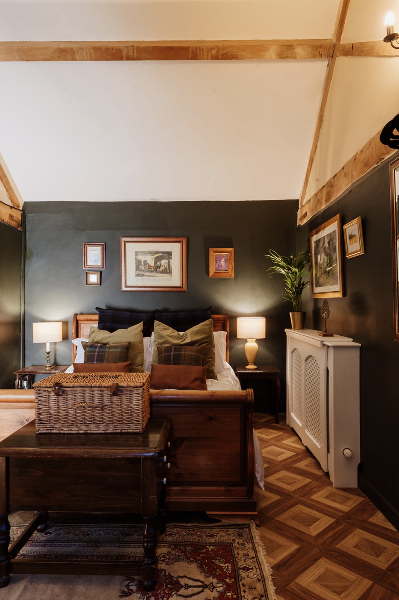 Warmly lit Pool House bedroom with a timber bed, layered cushions and exposed beams