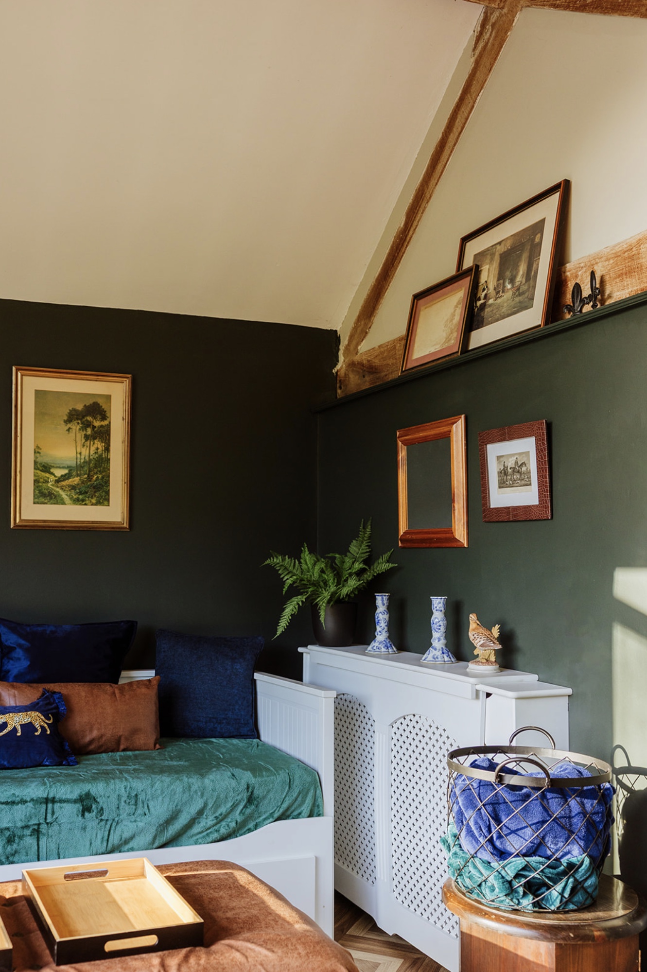 Pool House daybed corner with dark green walls, framed art and layered blue and rust cushions